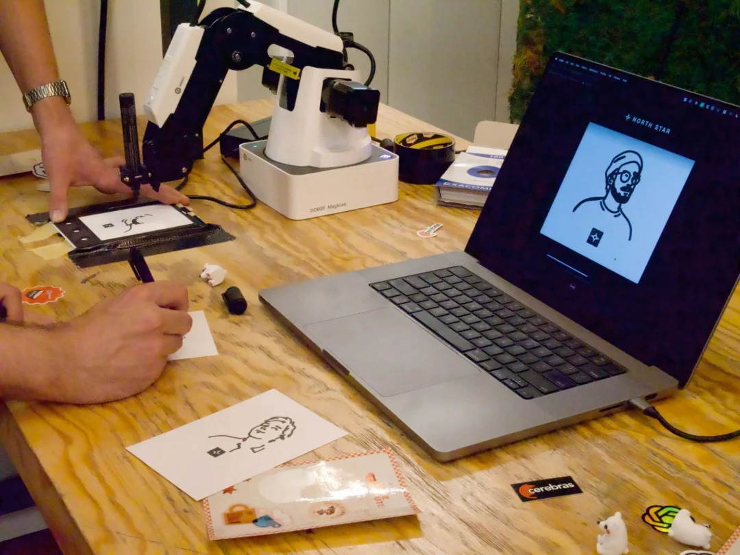 North Star DOBOT Magician robot drawing portraits on paper beside a laptop showing the line drawing.