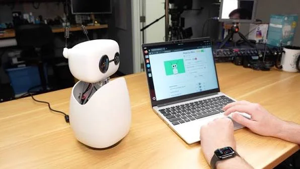 Reachy Mini robot on a table beside a laptop.